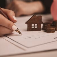 Close up wooden toy house with Woman signs a purchase contract or mortgage for a home, Real estate concept.