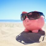 Summer piggy bank with sunglasses on the beach