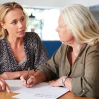 Female Friend Helping Senior Woman To Complete Last Will And Testament At Home