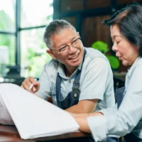 Elderly asian couple wearing apron smiling while reviewing document together at wooden table